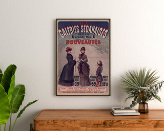 Vintage-Werbeplakat "Galeries sedanaises, Neuheiten", gerahmt über einer Holzkommode, zwischen Pflanzen.