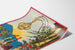 Vintage-Weinplakat – Au bon vin d’Alsace – Hansi, auf gebogenem Papier gezeigt, perspektivische Ansicht.