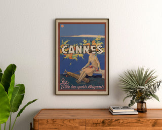 Vintage-Poster "Cannes, die eleganten Sportarten", gerahmt über einer Holzkommode, zwischen Pflanzen.