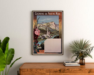 Vintage-Poster Lourdes, Chemins de fer du Midi, gerahmt über einer hölzernen Kommode, zwischen Pflanzen.