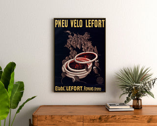 Vintage-Plakat Fahrradreifen Lefort, gerahmt über einer Holzkommode, zwischen Pflanzen.