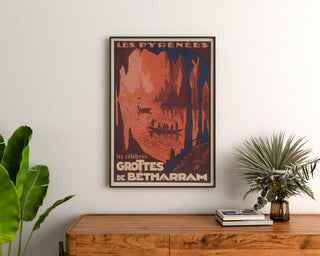 Vintage-Poster Pyrénées, Grottes de Bétharram, gerahmt über einer hölzernen Kommode, zwischen Pflanzen.